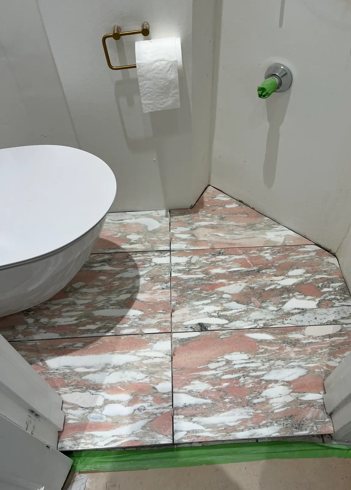 Samme toiletkrog med nyt gulv i rosa marmorfliser lagt helt ind i hjørnet, væghængt toilet, messingholder og grøn tapelinje langs soklen