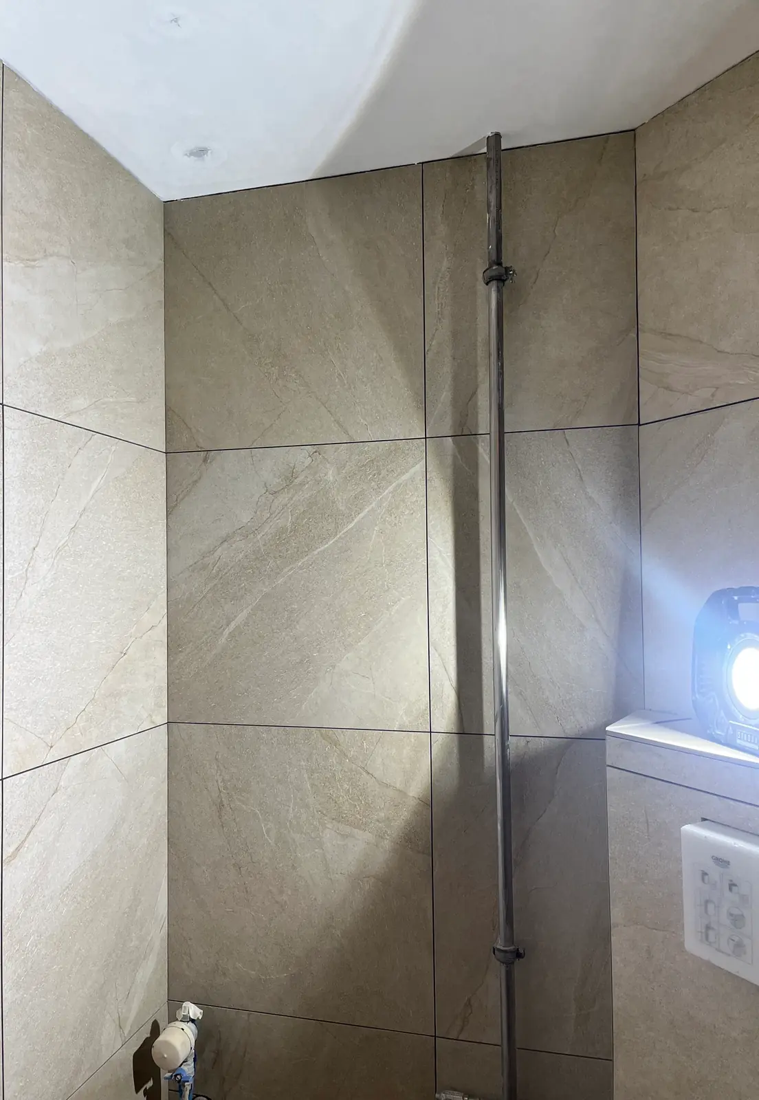 Beige storformatfliser oppe på begge vægge, hvidmalet loft med spotudskæring og en arbejdslampe på flisehylden